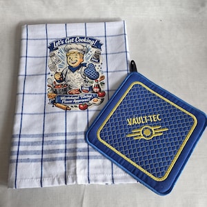 Peut inclure: Un torchon de cuisine blanc à carreaux bleus avec une illustration de chef et le texte Let's Get Cooking! Wasteland Tested, Flavor Approved! accompagné d'une manique carrée bleue matelassée avec un liseré jaune et le logo Vault-Tec.