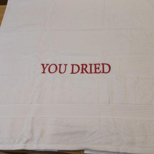 Pu&ograve; includere: Asciugamano da bagno bianco con la scritta ricamata "YOU DRIED" in rosso. L'asciugamano ha una superficie strutturata e una fascia decorativa nella parte inferiore. Un accessorio da bagno semplice e umoristico.
