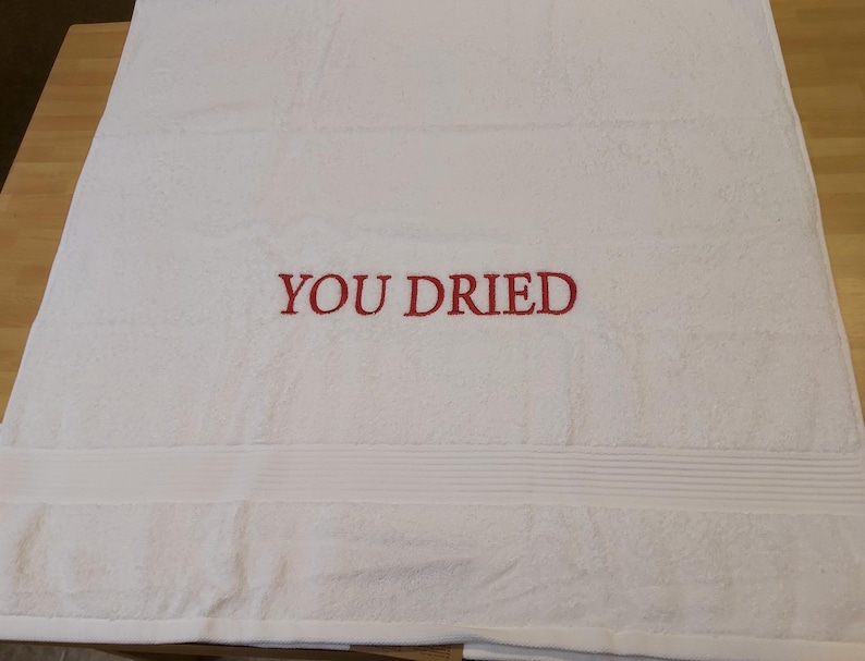 Pu&ograve; includere: Asciugamano da bagno bianco con la scritta ricamata "YOU DRIED" in rosso. L'asciugamano ha una superficie strutturata e una fascia decorativa nella parte inferiore. Un accessorio da bagno semplice e umoristico.