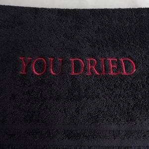 Pu&ograve; includere: Asciugamano nero con la scritta rossa ricamata "YOU DRIED". L'asciugamano ha una superficie strutturata e un design semplice, adatto per l'uso in bagno.