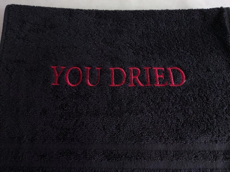 Pu&ograve; includere: Asciugamano nero con la scritta rossa ricamata "YOU DRIED". L'asciugamano ha una superficie strutturata e un design semplice, adatto per l'uso in bagno.