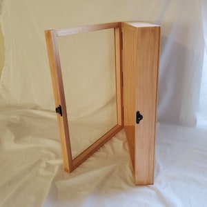 May include: A wooden display case with a glass front and a hinged door. The case is made of light wood and has a simple design.