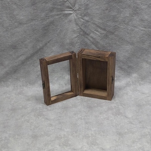 May include: A wooden box with a hinged lid, open to reveal an empty interior. The box is made of dark brown wood with a natural grain pattern.