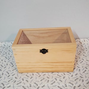 May include: A wooden box with a clear glass lid and a black metal latch. The box is made of light wood and has a natural finish.