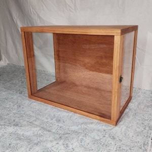 May include: A wooden display case with glass panels on three sides. The case has a simple design with a light wood finish.