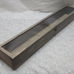 May include: A long, rectangular wooden display box with a glass top. The box is stained a dark gray color and has a small metal latch on the side.