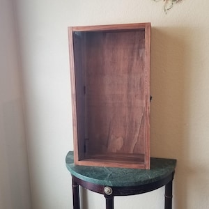 May include: A rectangular wooden display case with a dark brown finish, mounted on a green marble-topped table with dark legs. A decorative butterfly is affixed to the wall above the case.