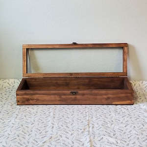 May include: A wooden display case with a glass top. The case is open and the interior is empty.