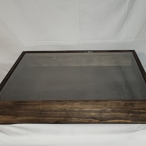 May include: A dark brown wooden display case with a glass top. The case has a simple design and is perfect for showcasing collectibles or other items.