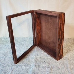 May include: A dark brown wooden display case with a glass door. The case is open and the interior is empty.