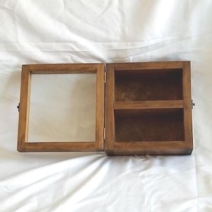 May include: A wooden display case with a glass front and two shelves. The case is closed and has a brown finish.