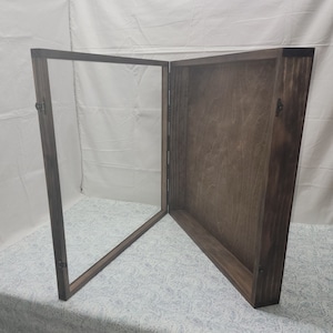 May include: A wooden display case with a hinged, clear glass door. The case is open, revealing the interior. The wood has a dark stain, and the case is designed to showcase items. The case is sitting on a patterned surface.