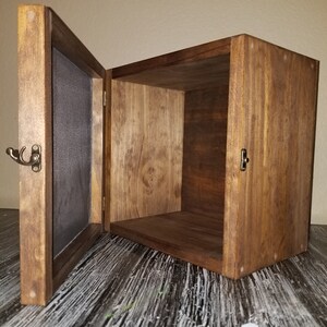 May include: A wooden box with a hinged door and a metal latch. The box is stained a dark brown color and has a natural wood grain. The door is open and the inside of the box is empty.