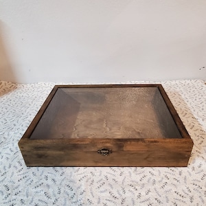 May include: A wooden display box with a glass top and a metal latch. The box is stained a dark brown color and has a rustic appearance.