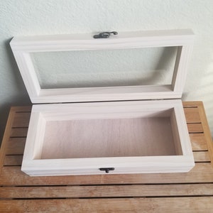 May include: A white wooden box with a glass top and a black latch. The box is open and empty.