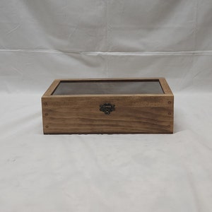 May include: A wooden box with a glass top and a metal latch. The box is light brown in color and has a rustic finish.