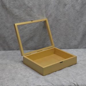 May include: A wooden display box with a clear glass lid, open to reveal the interior. The box is a light yellow color, with a rectangular shape. The lid is hinged and slightly ajar, showcasing the inside of the box.