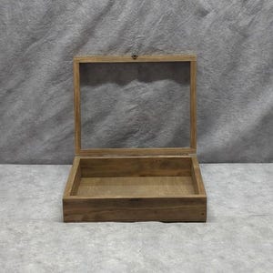 May include: A wooden display box with a clear glass top, open to reveal the interior. The box is made of light-colored wood and has a simple, rectangular design. The glass top is hinged and secured with a small clasp.