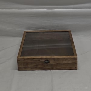 May include: A wooden display case with a glass top and a metal latch. The case is stained a dark brown color and has a rustic appearance.