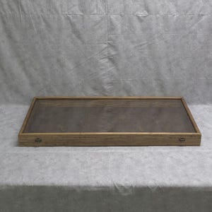 May include: A wooden display case with a glass top. The case has a brown wood finish and two small metal handles.