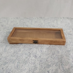 May include: A rectangular wooden display box with a glass top and a metal latch. The box is made of light brown wood and has a natural finish.