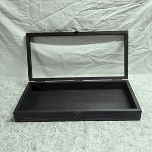 May include: A black wooden display case with a glass top. The case is open and empty.