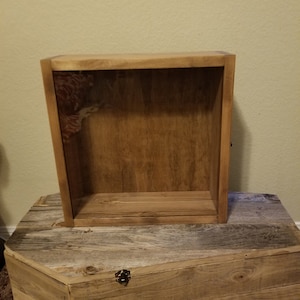 May include: A wooden box with a single shelf inside. The box is made of natural wood with a light brown stain. The box is sitting on a wooden surface.