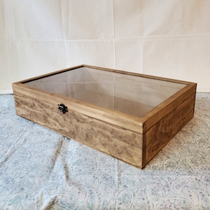 May include: A wooden display box with a glass top and a metal latch. The box is stained a light brown color and has a natural wood grain.