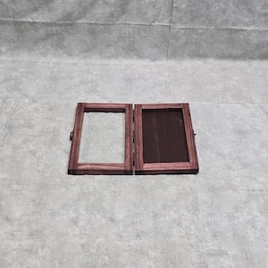 May include: Two wooden picture frames with a dark purple stain. The frames are hinged together and are closed.