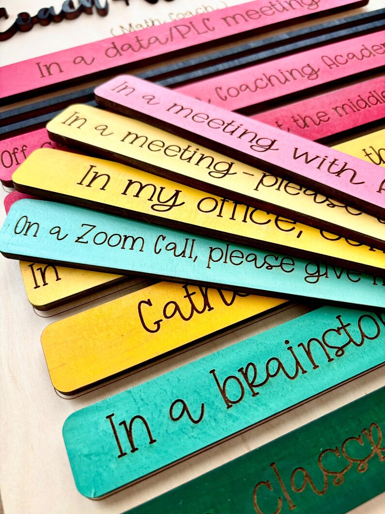 May include: A set of colorful wooden signs with different phrases for a teacher's classroom. The phrases include "In a data/PLC meeting", "In a meeting - please give me a few minutes", "In my office, on a Zoom call, please give me a few minutes", "Gather", "In a brainstorming session", and "Classroom".