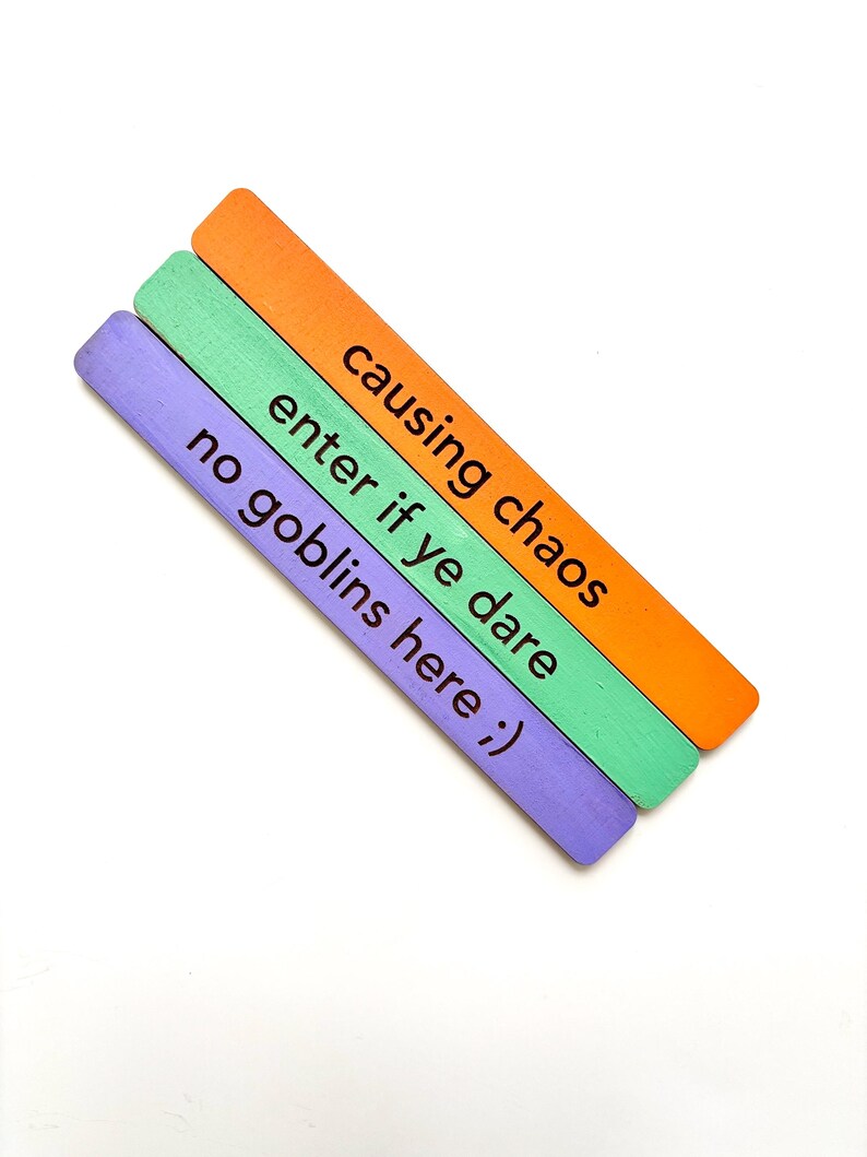 May include: Three wooden sticks painted in purple, green, and orange with the text "causing chaos enter if ye dare no goblins here ;)" written on them.