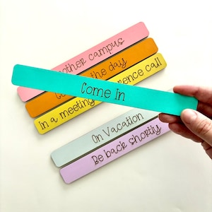 May include: A set of five wooden door hangers with different colored backgrounds and messages. The messages are "Other Campus", "Gone for the Day", "In a Meeting", "Come In", "On Vacation", and "Be Back Shortly".