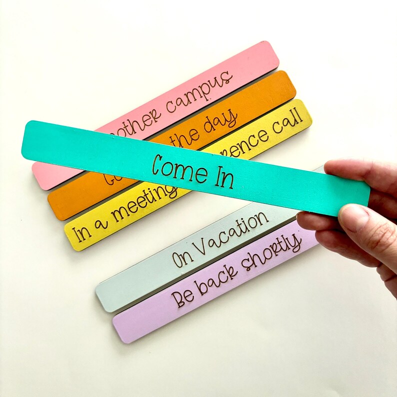 May include: A set of five wooden door hangers with different colored backgrounds and messages. The messages are "Other Campus", "Gone for the Day", "In a Meeting", "Come In", "On Vacation", and "Be Back Shortly".