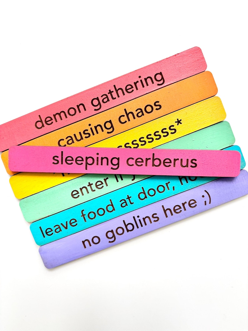 May include: A set of six colorful wooden sticks with different phrases written on them. The phrases are: "demon gathering", "causing chaos", "sleeping cerberus", "enter", "leave food at door, ho", and "no goblins here ;)".