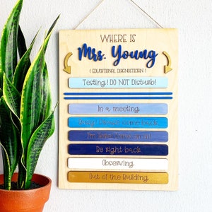 May include: A wooden sign with the text "WHERE IS Mrs. Young (EDUCATIONAL DIAGNOSTICIAN)" and a sliding indicator with the options "Testing! DO NOT Disturb!", "In a meeting", "Busy! Please come back.", "I'm here! Come on in!", "Be right back", "Observing", and "Out of the Building".