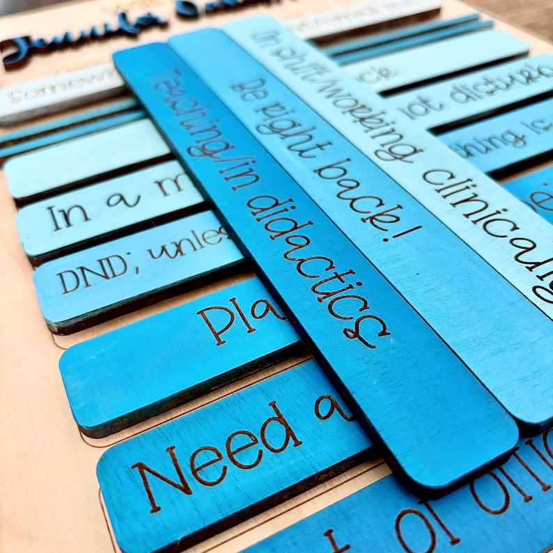 May include: A set of blue wooden tiles with various phrases engraved on them, including "In a moment", "DND; unless", "Playing in didactics", "Be right back!", "I'm not doing clinically", "Something is wrong", and "Need a".