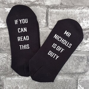 May include: A pair of black socks with white text. One sock says "If you can read this" and the other sock says "Mr Nicholls is off duty".