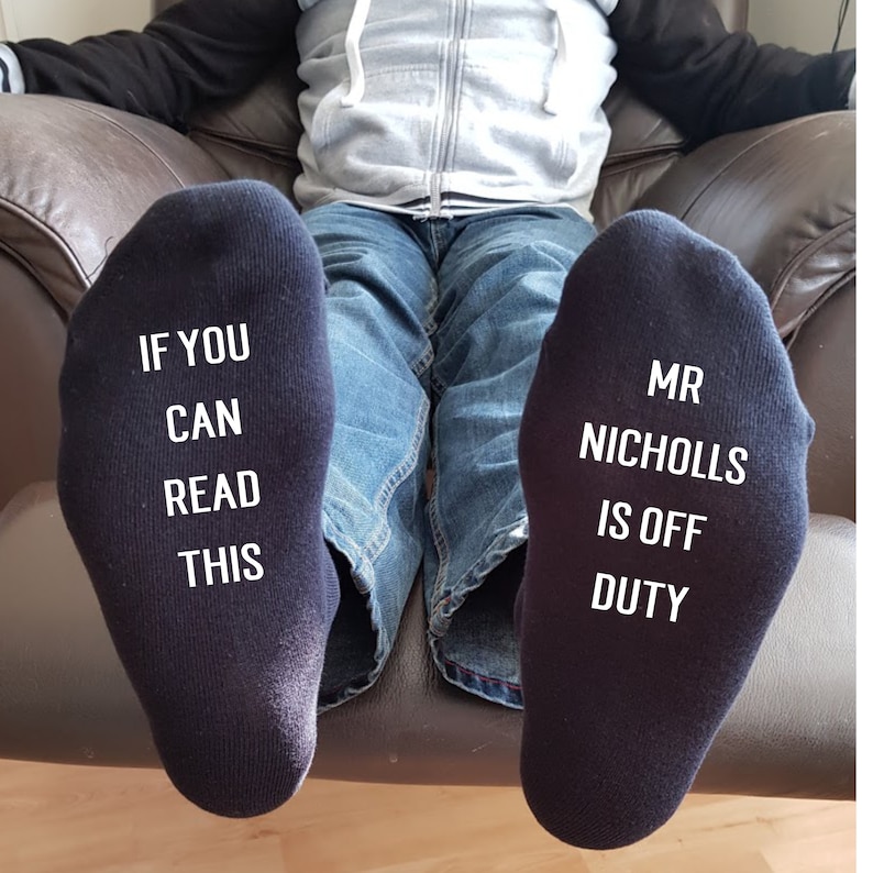 May include: A pair of black socks with white text. One sock reads "If you can read this" and the other sock reads "Mr Nicholls is off duty".