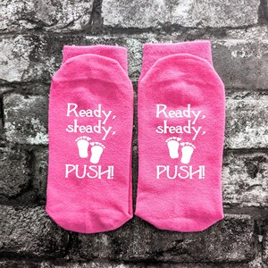 May include: A pair of pink ankle socks with white text that reads "Ready, steady, push!" and a graphic of two baby footprints with hearts.