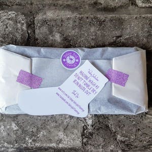 May include: A white tissue paper package with a purple sticker that says "Dalay Dot Flamingo" and a white card with purple text that says "MACHINE WASH 40 DO NOT TUMBLE DRY IRON INSIDE OUT" and a website address.