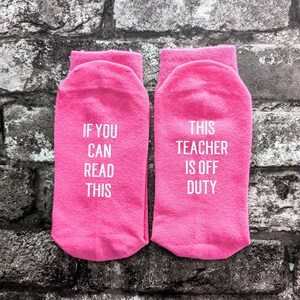 May include: A pair of pink socks with white text. One sock says "If you can read this" and the other sock says "This teacher is off duty".