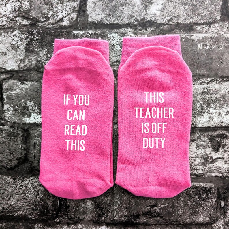 May include: A pair of pink socks with white text. One sock says "If you can read this" and the other sock says "This teacher is off duty".