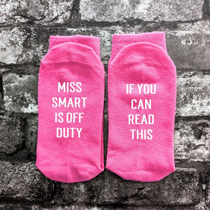 May include: A pair of pink socks with white text. One sock says "Miss Smart is off duty" and the other sock says "If you can read this".
