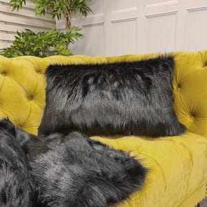 May include: Two black faux fur throw pillows on a yellow velvet sofa. The pillows are rectangular and have a soft, fluffy texture.