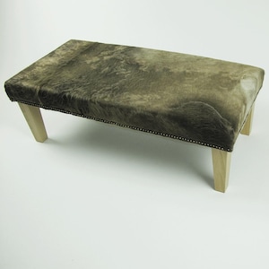 May include: A brown cowhide bench with wooden legs. The bench has a tufted design and a natural, rustic look.