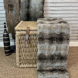 May include: A brown and gray faux fur throw blanket with a woven wicker storage basket and a matching faux fur pillow.