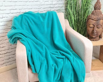 May include: A teal blue fleece throw blanket draped over a light beige armchair. The blanket is soft and plush, perfect for adding warmth and comfort to any room.