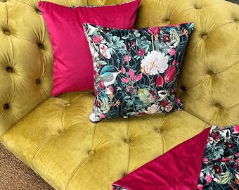 May include: A mustard yellow velvet sofa with two pink velvet throw pillows and a throw blanket with a floral print. The floral print features tropical plants, birds, and a geometric pattern.