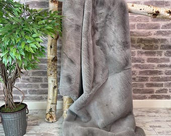 May include: A soft, grey faux fur throw blanket draped over a branch. The blanket has a fluffy texture and is perfect for adding warmth and style to any room.