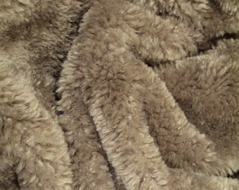 May include: Close-up of a soft, brown faux fur fabric. The fabric has a fluffy texture and is ideal for making blankets, throws, or clothing.